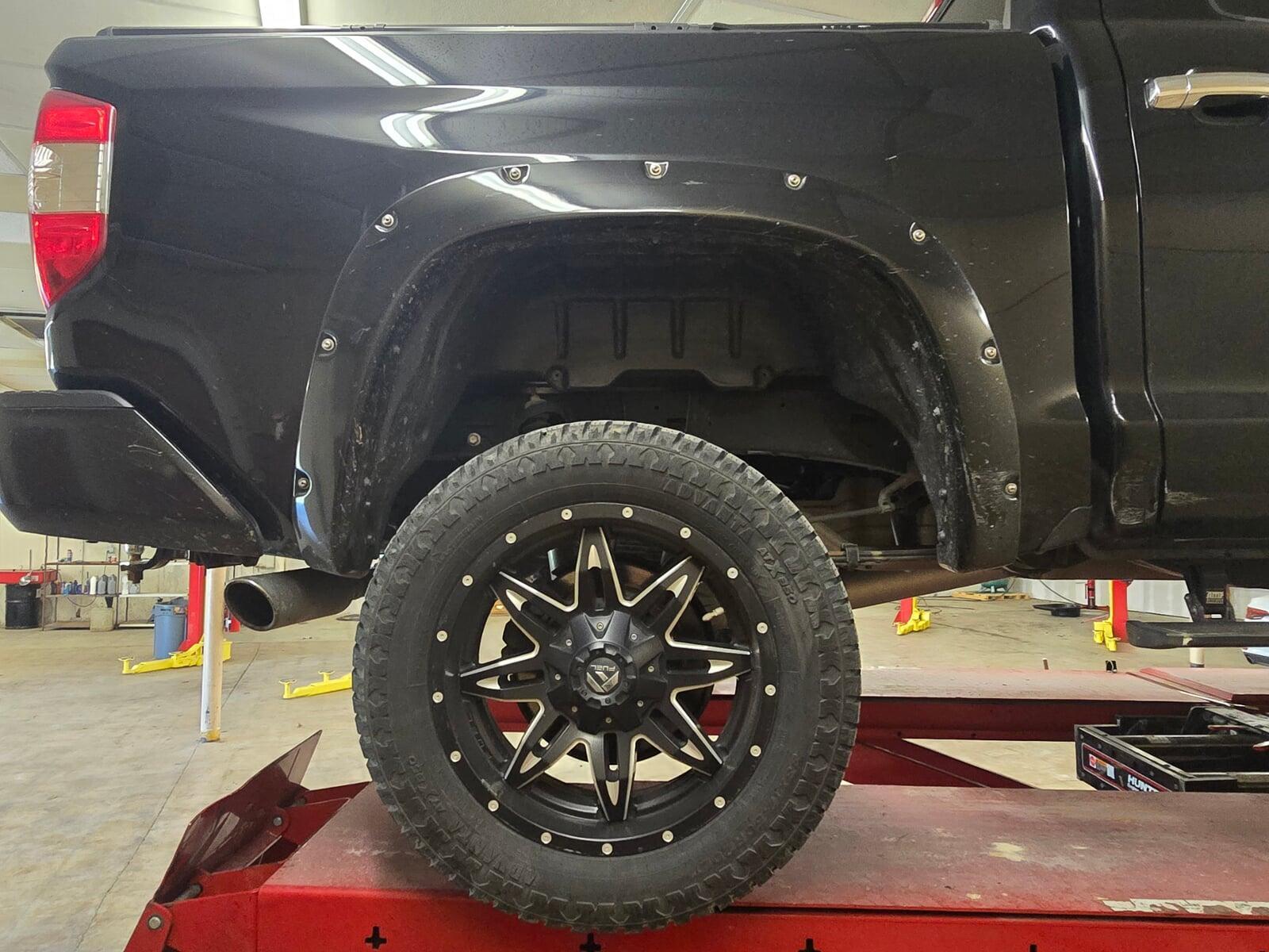 Truck on alignment rack with rear wheel and suspension damage.